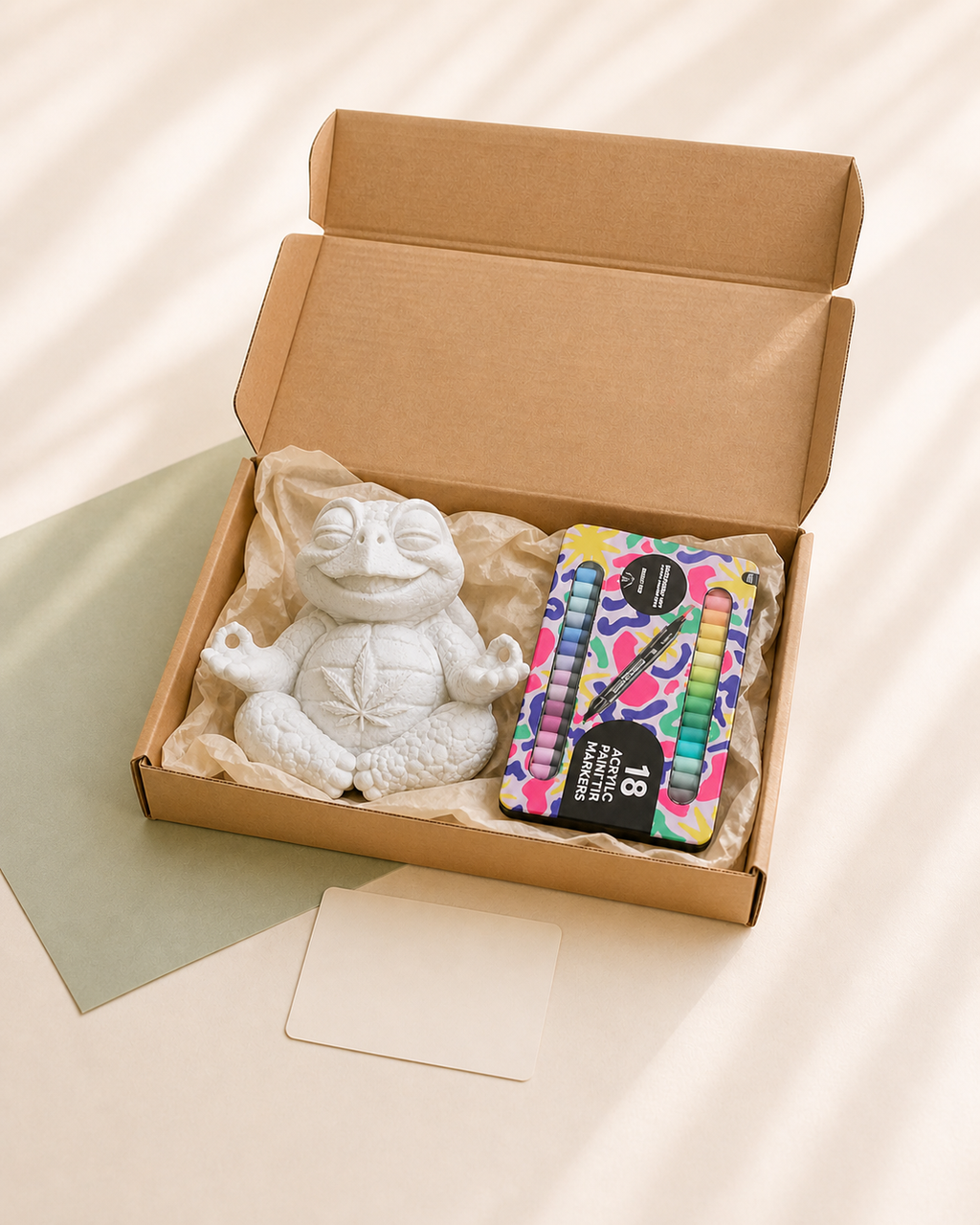 Offene Kraftpapierbox mit einer unbemalten Shellax Figur, 18 Acrylmarkern und neutraler Karte.