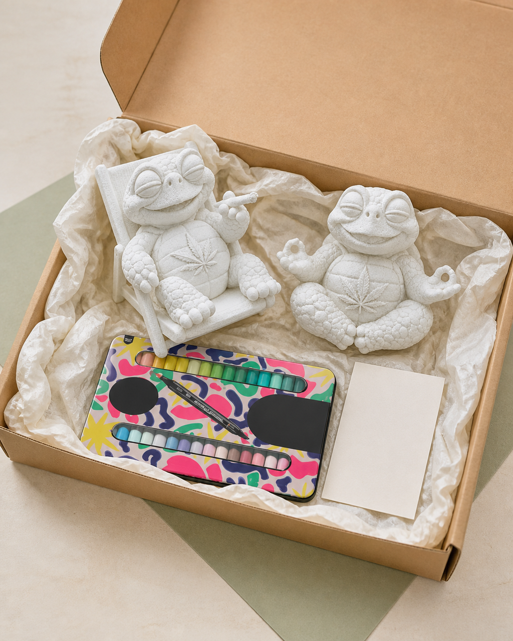 Offene Kraftpapierbox mit zwei unbemalten Shellax Figuren, 18 Acrylmarkern und neutraler Karte.